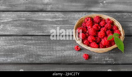 Lamponi freschi con una foglia in un cestino di vimini su un tavolo di legno. Banner. Spazio per il testo. Spazio di copia Foto Stock