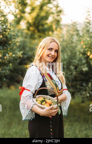 Giovane donna bionda in serbo tradizionale con un cesto di pere fresche Foto Stock