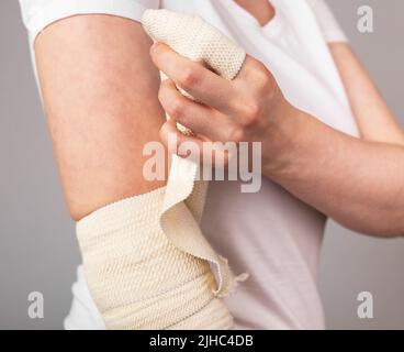 Donna che avvolge il bendaggio elastico intorno al gomito doloroso. Avvolgimento a compressione. Lesione del braccio, uso eccessivo, infiammazione, conseguenze dell'artrite. Concetto di assistenza sanitaria. Foto di alta qualità Foto Stock