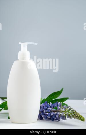 Bottiglia cosmetica con lozione e fiori lupino su sfondo grigio. Cosmetici naturali per la cura del corpo e del viso. Concetto di prodotti biologici spa, relaxati Foto Stock