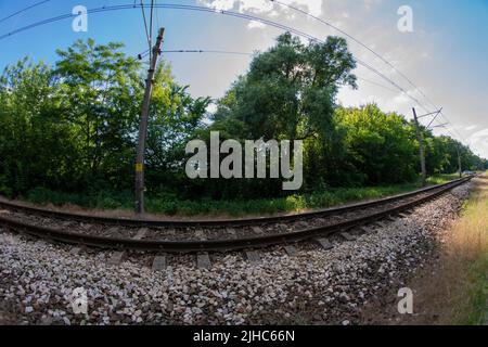 Binari ferroviari e strada sterrata attraverso la lente fisheye UWA in una giornata di sole. Foto Stock