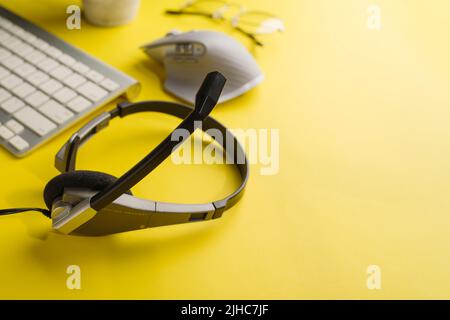 Dispositivi moderni per l'ufficio e l'ufficio domestico. Computer portatile, cuffie, mouse su sfondo giallo chiaro. Pubblicità, banner. Non ci sono persone in Foto Stock