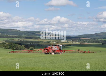 Un Bateman 4000 irrorando un campo di Barley in Summer Sunshine con vista su Un paesaggio panoramico in Aberdeenshire Foto Stock