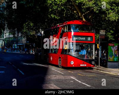 Il Red London Bus emerge dalle ombre nel centro di Londra. Un autobus New Routemaster n. 8 per Bow Church è parcheggiato in parte all'ombra in una strada londinese. Foto Stock