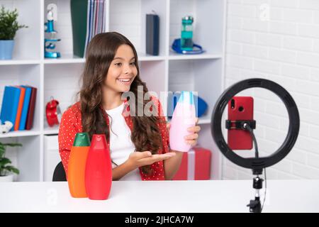 Bambino vlogger fare video blog sul telefono. Blogging weblog e vlog. Teen ragazza blogger influencer tenere balsamo capelli o shampoo bottiglia per sociale Foto Stock