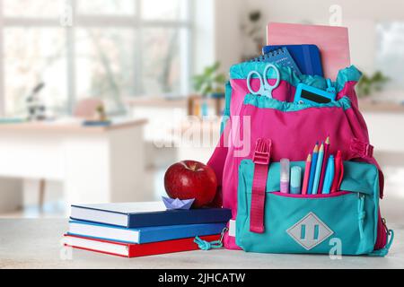 Zaino scuola con cancelleria, mela e libri sul tavolo in classe Foto Stock