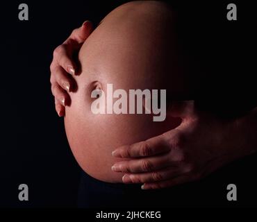 Donna incinta che tiene esposta la pancia su sfondo nero. Dettaglio di una donna incinta che tiene esposto il ventre su sfondo nero. Foto Stock