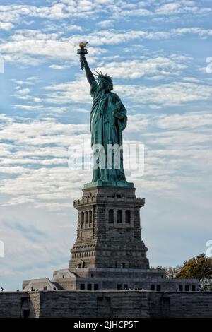 NEW YORK, NY - 04 NOV 2019: Statua della libertà e piedistallo con turisti intorno alla base in una giornata di cielo nuvoloso blu. Foto Stock