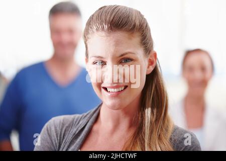 Giovani professionisti che entrano sul posto di lavoro. Primo piano di una giovane donna d'affari attraente in piedi con fiducia con i suoi collaboratori in background. Foto Stock