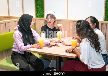 Giovani donne asiatiche che hanno un grande tempo in un caffè. Bere succo d'arancia e socializzare. Foto Stock