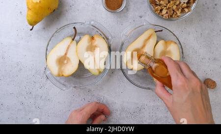 Pere al forno con noci, miele e cannella, primo piano su sfondo rustico, colazione o dessert perfetto, piatto laico, mani donna Foto Stock