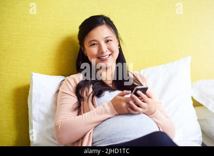 Ho avuto modo di tenere in contatto con i miei cari sulla mia gravidanza. Ritratto di una donna incinta usando un cellulare a casa. Foto Stock