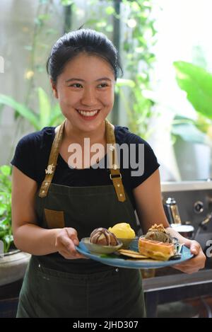 Ragazza vietnamita che serve gelato fatto in casa con waffle in una caffetteria. Foto Stock