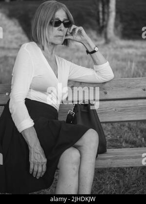 senior fit elegante donna vestita blaka dn bianco indossare occhiali da sole godere della natura in estate Foto Stock