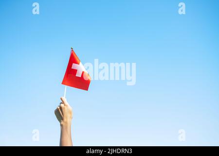 Mano che tiene bandiera Svizzera su sfondo blu cielo. Festa nazionale della Svizzera e buone celebrazioni Foto Stock