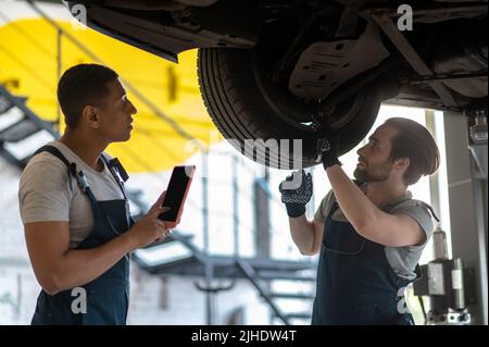 Tecnici al servizio auto che fanno l'ascensore per l'ispezione dell'auto Foto Stock