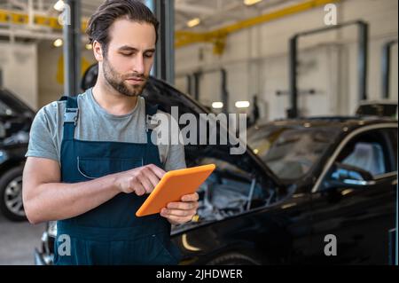 Meccanico automatico che guarda il tablet in piedi in officina Foto Stock