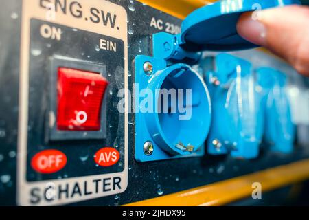 Presa di alimentazione blu sul corpo di un generatore elettrico a benzina in primo piano. Mancanza di elettricità nella rete Foto Stock