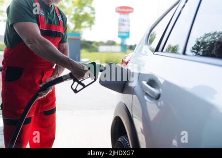 Lavoratore senior in piedi sulla stazione di servizio e auto di rifornimento. Foto Stock