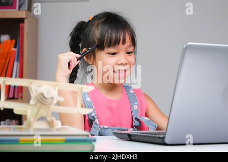 Sorridente ragazza asiatica che studia in linea avendo videochiamata classe distante con l'insegnante che usa il laptop. Ragazza felice imparando l'inglese in linea con il laptop a. Foto Stock