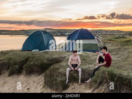 Garrylucas, Cork, Irlanda. 17th luglio 2022. In una calda serata estiva, i campeggiatori Joseph Lawlor di Kinsale e Willie Burke di Cobh si rilassano sulle dune di sabbia mentre il sole tramonta a Garrylucas, Co. Cork, Irlanda. - Credit; David Creedon / Alamy Live News Foto Stock