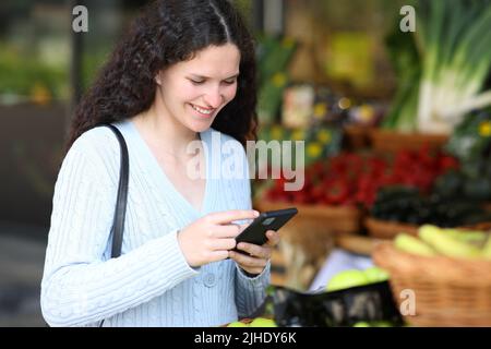 Cliente che utilizza uno smartphone in piedi in un negozio di alimentari Foto Stock