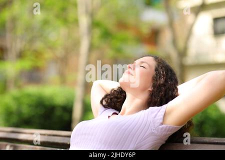 Donna rilassata che riposa con le braccia sulla testa seduta in una panca in un parco Foto Stock