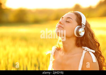 Donna rilassata meditando con cuffie wireless in un campo di grano al tramonto Foto Stock