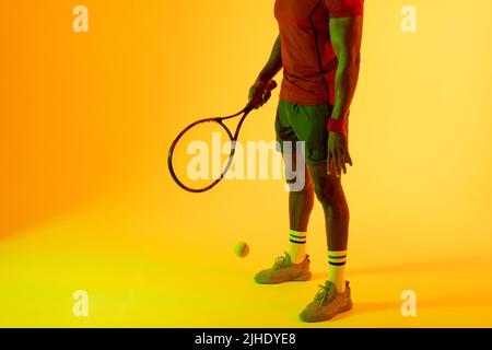 Immagine della sezione bassa del giocatore di tennis maschile afroamericano con illuminazione gialla Foto Stock