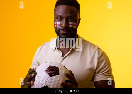Immagine di un tifoso di calcio maschile africano americano con bandiera d'inghilterra in luce gialla Foto Stock