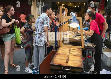 I turisti indiani e occidentali in una bancarella di spuntini in Domenica Walking Street Market, Thalang Road, zona della Città Vecchia a Phuket Town (Chinatown), Phuket, Thailandia Foto Stock