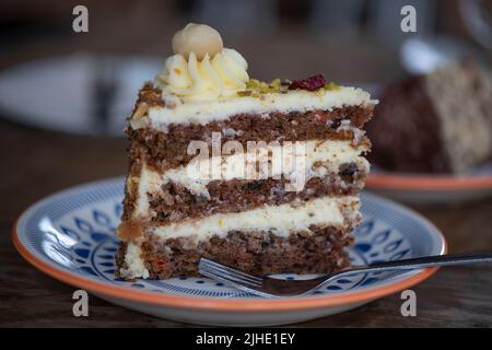 Fetta di gustoso dolce a tre strati di carote dolci e umide farcite di noci pecan tostate e deliziosa glassa di formaggio cremoso servita su un piatto di ceramica Foto Stock