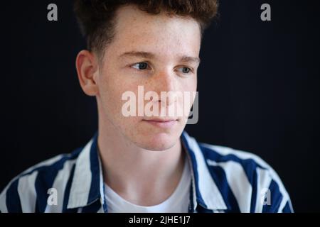 Ritratto di bel giovane uomo pensieroso con capelli zenzero e frane guardando via su sfondo nero, primo piano Foto Stock