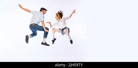 Ritratto di giovane coppia attiva, uomo e donna, ballando, saltando isolato su sfondo bianco studio. Volantino Foto Stock