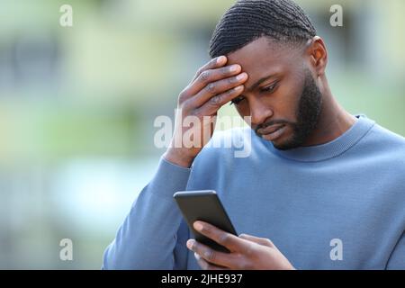 Uomo nero preoccupato che controlla lo smartphone per strada