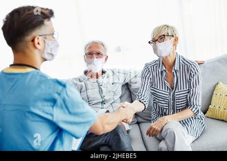 nurse medico cura anziana caregiver aiuto pensione assistenza casa maschera corona infermiere handshake uomo infermieristico Foto Stock