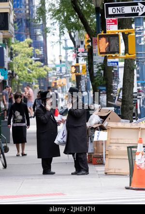 Due ebrei Hasidic sembrano parlare contemporaneamente l'uno con l'altro e anche usando i loro telefoni cellulari. Su Lee Avenue a Brooklyn, New York. Foto Stock