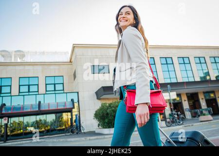 Ritratto di una donna in viaggio d'affari che cammina in una stazione ferroviaria o aeroporto andando al cancello d'imbarco con bagaglio a mano Foto Stock
