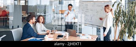 L'uomo e la donna asiatici conducono una riunione per i dipendenti vicino a una lavagna a fogli mobili e spiega la strategia di lavoro Foto Stock