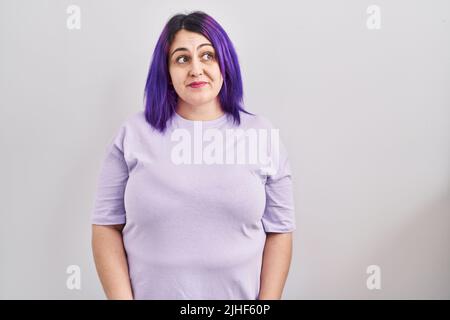 Plus size donna con capelli viola in piedi su sfondo isolato sorridendo guardando lateralmente e fissando via pensando. Foto Stock