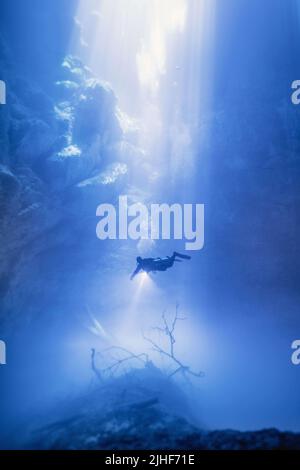 Un subacqueo è raffigurato in un fascio di luce solare che esplora la grotta subacquea. TULUM, MESSICO. QUESTE caverne ultraterrene catturate nelle grotte sottomarine del Messico Foto Stock