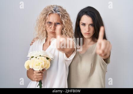 Madre e figlia che tengono bouquet di fiori bianchi puntando con il dito su ed espressione arrabbiata, non mostrando alcun gesto Foto Stock