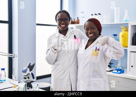 Due donne africane che lavorano al laboratorio di scienziato puntando il dito ad un auto sorridente felice e orgoglioso Foto Stock