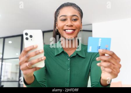 Eccitata donna afroamericana che acquista online, detiene carta di credito bancaria e smartphone, inserisce dati e effettua acquisti online, donna multirazziale utilizzando l'app e-banking Foto Stock