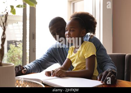 Immagine di felice padre e figlia afroamericana con vista disabilità lettura in braille Foto Stock