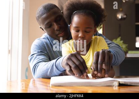 Immagine di felice padre e figlia afroamericana con vista disabilità lettura in braille Foto Stock