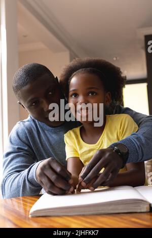 Immagine verticale di felice padre e figlia afroamericana con lettura di disabilità visiva Foto Stock
