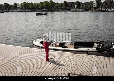 Una vista elevata di una donna che tiene la linea di ormeggio di un motoscafo su un canale in una giornata calda e soleggiata ad Amsterdam, Paesi Bassi. Foto Stock
