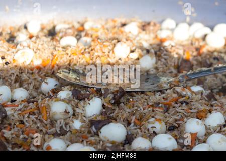 Pilaf con uova di quaglia in una padella grande durante la cottura, primo piano Foto Stock