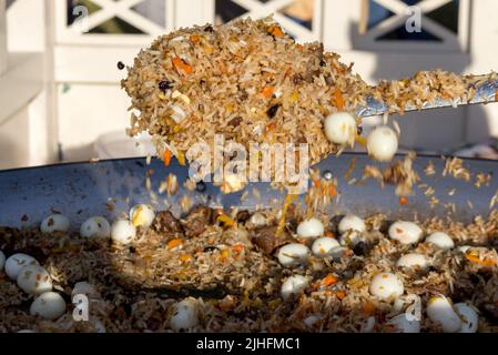 Pilaf con uova di quaglia in una padella grande durante la cottura, primo piano Foto Stock